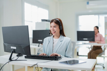 Happy businesswoman with headphones working on PC in call center office, young female technical...
