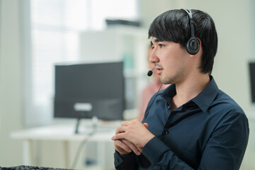 Happy businessman with headphones working on PC in call center office, young male technical support...