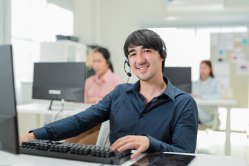 Happy businessman with headphones working on PC in call center office, young male technical support...
