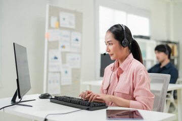 Happy businesswoman with headphones working on PC in call center office, young female technical...