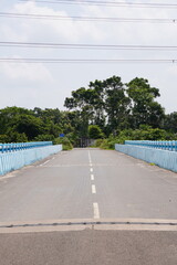 A road leading to a bridge given the surrounding lush greenery and power lines overhead