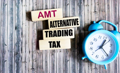 Clipboard with the text AMT Alternative Trading Tax placed next to laptop, calculator, and black pen on a gray desk .