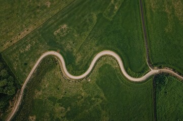 Fototapeta premium Curvy country road cutting through farmland captured from above, representing rural simplicity and natural terrain.