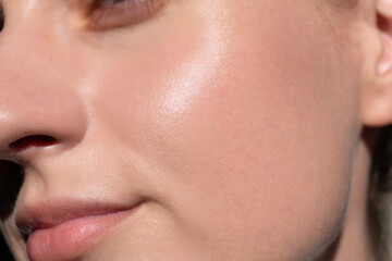 Macro view of glowing woman’s cheek, nose and lips in sunlight. Smooth texture, healthy...