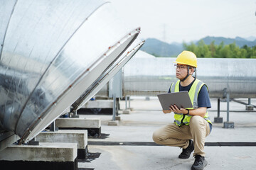 asian engineer working on laptop with  external unit of commercial air conditioning and ventilation system installed on industrial building roof