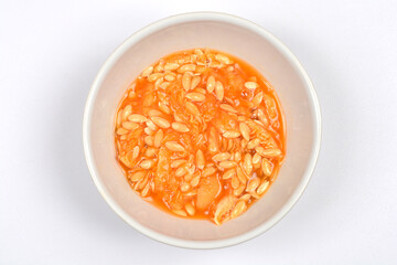 A small white bowl containing a mixture of orange cantaloupe flesh and numerous seeds is centered...