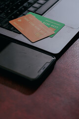 Laptop with mobile phone and credit cards on leather maroon background, top view, closeup. Online...