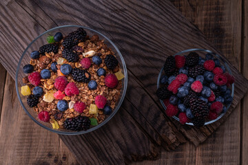 Mix of summer forest berries in a plate. Mix of berries and granola. Glass bowls with berries. Old wooden background. Top.