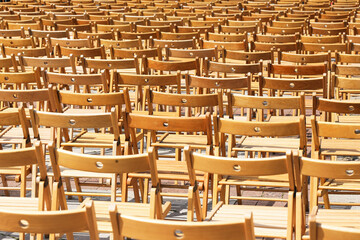 Many wooden chairs arranged in rows. Outdoor seating preparation for event. Brown folding chairs on...