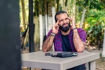 Intensely focused Colombian man in plaid shirt reacting with frustration while pointing at phone at...