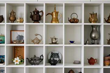 Decorative display of vintage teapots and teacups arranged in white cubical shelving unit,...