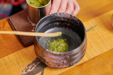 Elegant tea ceremony with woman dipping bamboo stir stick into green tea, surrounded by black teapot, utensils, and custom tea accessories in a contemporary setting
