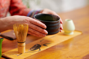 Serene tea ceremony with woman holding black teacup and bamboo whisk, surrounded by traditional...