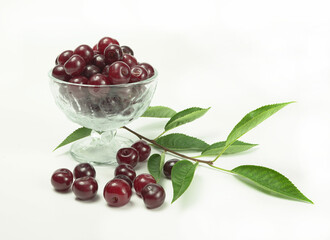 Berries of red, ripe cherries, cherries in a glass vase, berries of cherries and a branch of cherries lie nearby, on a white background.
