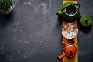 Tea set with green teapot, floral bowl, and terracotta teapot, arranged on decorative mat against...