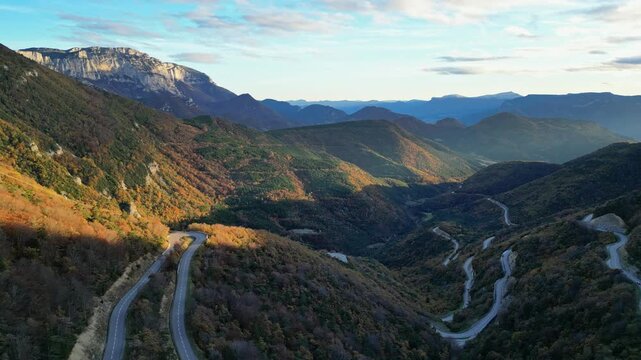  Winding mountain road in Vercors seen from Col de Rousset at sunset, cars driving through forested slopes in Drome region, southeastern France