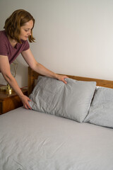 Woman holding a pillow with fresh clean pillowcases, grey cotton bed sheets