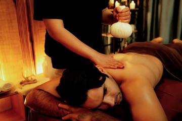 Hot herbal ball spa massage body treatment, masseur gently compresses herb bag on man body....