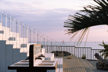 Staircase leading to a seaside restaurant at sunset, with a view of the calm ocean, a sailboat in...