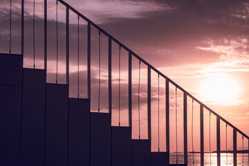 Modern staircase with minimalist railings silhouetted against a dramatic sunset sky by the water. The geometric lines and warm colors create a serene atmosphere perfect for conceptual themes.
