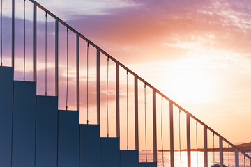 Modern staircase with minimalist railings silhouetted against a dramatic sunset sky by the water. The geometric lines and warm colors create a serene atmosphere perfect for conceptual themes.