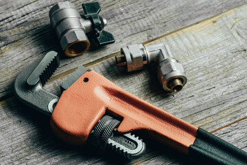 Adjustable pipe wrench and plumbing fittings on wooden background.