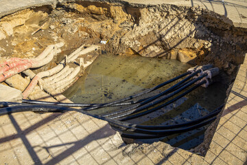 Hole in the ground with a lot of wires and cables coming out of it. The cables are black and the...