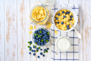 Healthy breakfast with corn flakes and blueberry on a white wooden table, top view.