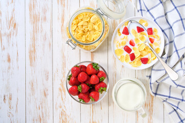 Healthy breakfast with corn flakes and strawberry on a white wooden table, top view.