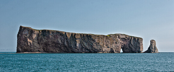 Famous limestone formation Percé Rock rising from the Gulf of Saint Lawrence in Quebec, Canada. Captured in clear daylight, showcasing its natural arch and rugged texture.
