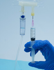 Gloved hand injecting medication from a syringe into an IV fluid bag via the designated port, with...