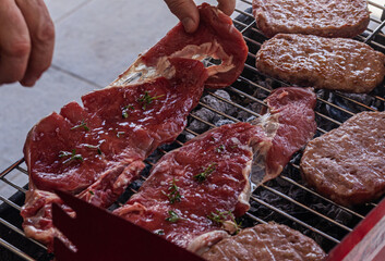 Juicy raw steaks seasoned with herbs and burger patties sizzling on a charcoal grill, captured during a backyard barbecue. Perfect for culinary visuals, grilling ads, or recipe illustrations