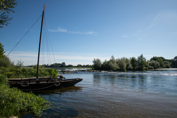 Traditional Loire boat moored on the banks of the Loire River at Meung-sur-Loire, France, under a clear blue sky with calm, reflective water.
