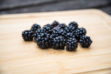 Fresh blackberries arranged on a rustic wooden board, highlighting natural texture and rich, dark color in a simple, organic composition.