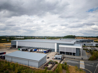 Large Modern Warehouse with Truck Loading Bays and Solar Panels on Roof, Surrounded by Countryside...