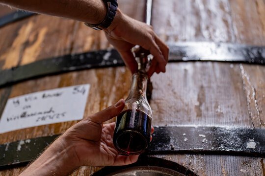 Gros plan sur de grandes cuves en bois align&eacute;es &agrave; l&rsquo;int&eacute;rieur d&rsquo;une installation artisanale ou industrielle d&eacute;di&eacute;e &agrave; la production de boissons. Vue sur un homme qui rempli une bouteille
