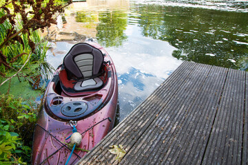 Red and black kayak moored against a wooden jetty on the River Lea, with calm water and natural surroundings creating a peaceful riverside scene.