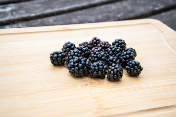 Fresh blackberries arranged on a rustic wooden board, highlighting natural texture and rich, dark color in a simple, organic composition.
