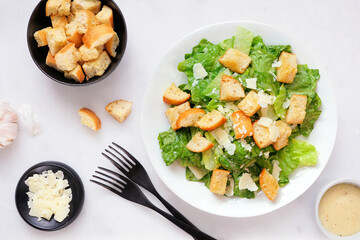 Classic Caesar salad with croutons and parmesan cheese. Above view table scene on a white marble background.