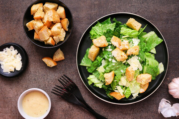 Traditional Caesar salad with croutons and parmesan cheese. Top down table scene on a dark background.