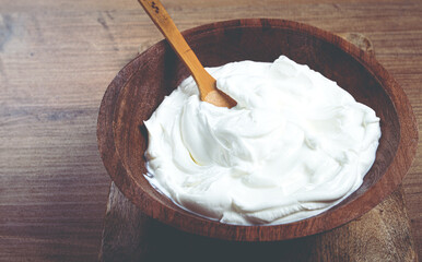 sour cream in a wooden bowl, on a wooden table, top view, close-up, no people,