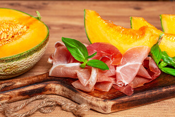 cantaloupe melon, with prosciutto, and fresh basil, on a wooden serving board, rustic style,