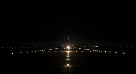 Airplane landing at night on a runway illuminated by lights creating a symmetrical composition