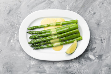 Tasty cooked asparagus served with sauce and lime on grey textured table, top view