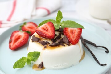 Tasty panna cotta with chocolate, strawberries, mint, caramel and vanilla pods on table, closeup