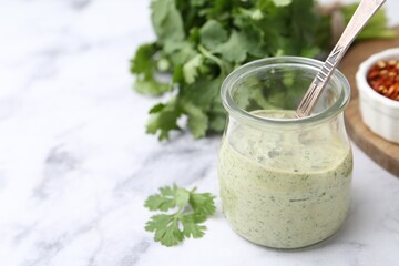 Tasty cilantro sauce and spoon in jar on light marble table, closeup. Space for text