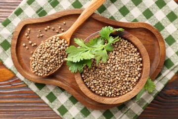 Coriander seeds in bowl, spoon and fresh cilantro sprigs on wooden table, top view