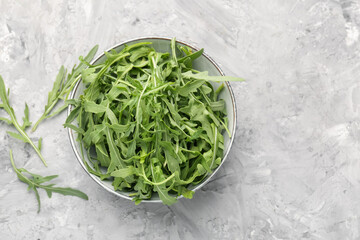 Fresh ripe green arugula leaves in bowl on grey table, flat lay. Space for text