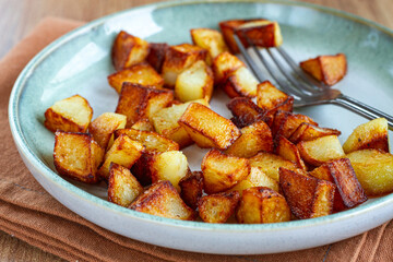 Golden crispy baked potatoes, on a green plate with a fork on a wooden table, no people