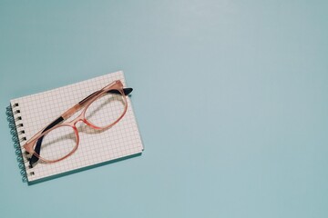 Pink glasses on a grid notepad against light blue. Perfect for themes of study, vision, creativity, and a focused workspace.